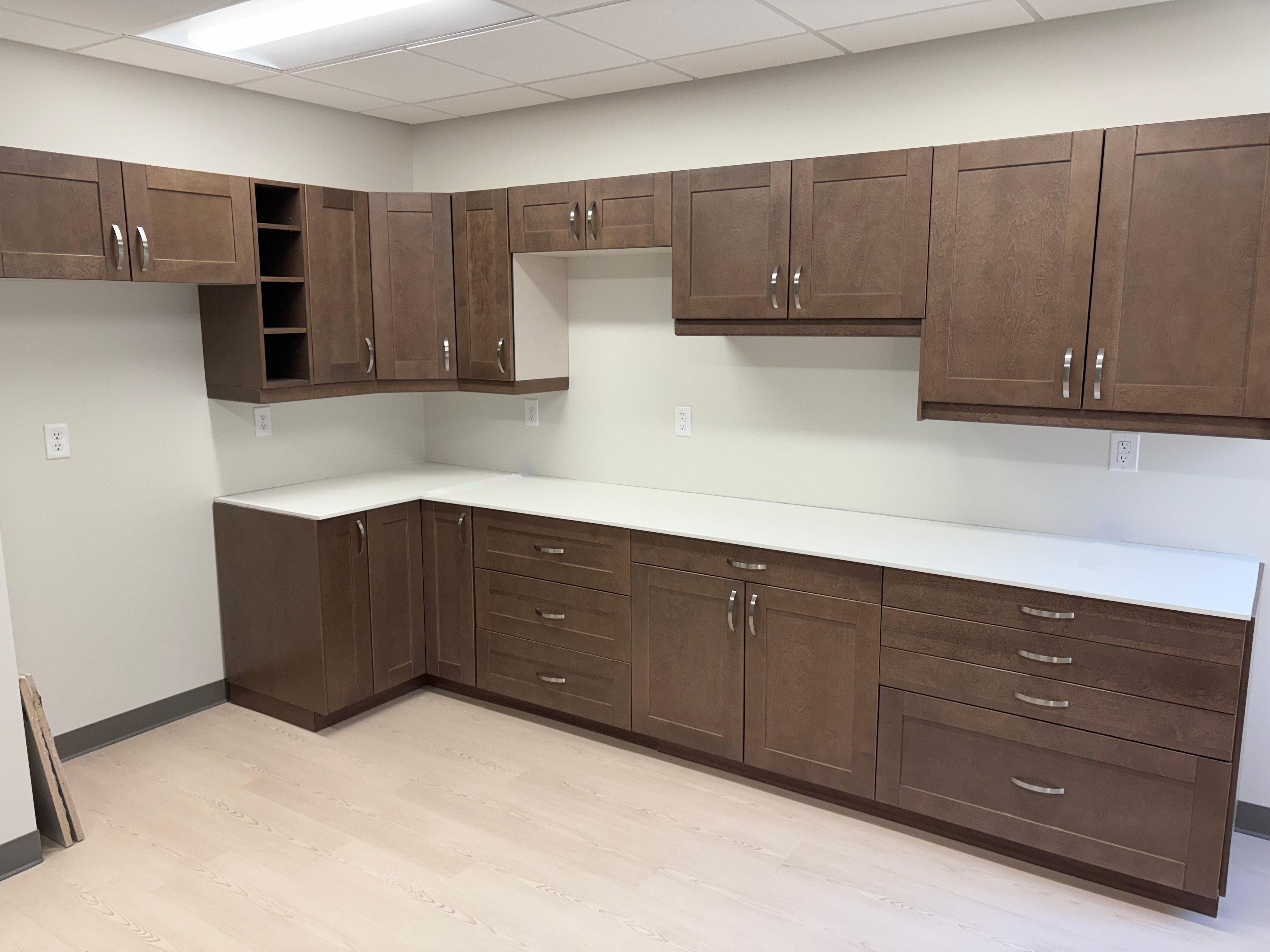 Commercial break room cabinetry with brown shaker doors and white solid surface countertops.